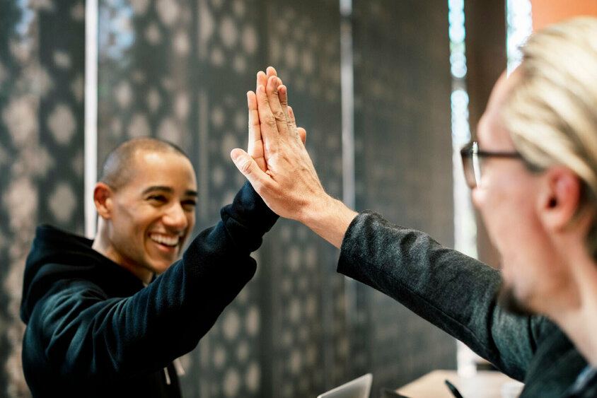 Jobs in Attendorn: Positive Arbeitsatmosphäre bei Gatzsch Schweißtechnik in Attendorn Zwei Kollegen geben sich in einem Büro High-Five, beide lächeln und wirken zufrieden. Die Szene symbolisiert Erfolg, Zusammenarbeit und eine positive Arbeitsatmosphäre. Im Hintergrund sind verschwommene Büroelemente zu sehen, die auf eine professionelle Umgebung hinweisen. Das Bild steht für die Vorteile und den Teamgeist, die Mitarbeiter bei Gatzsch Schweißtechnik in Attendorn erleben, und verdeutlicht die Bedeutung von gegenseitiger Unterstützung und Freude an der Arbeit.